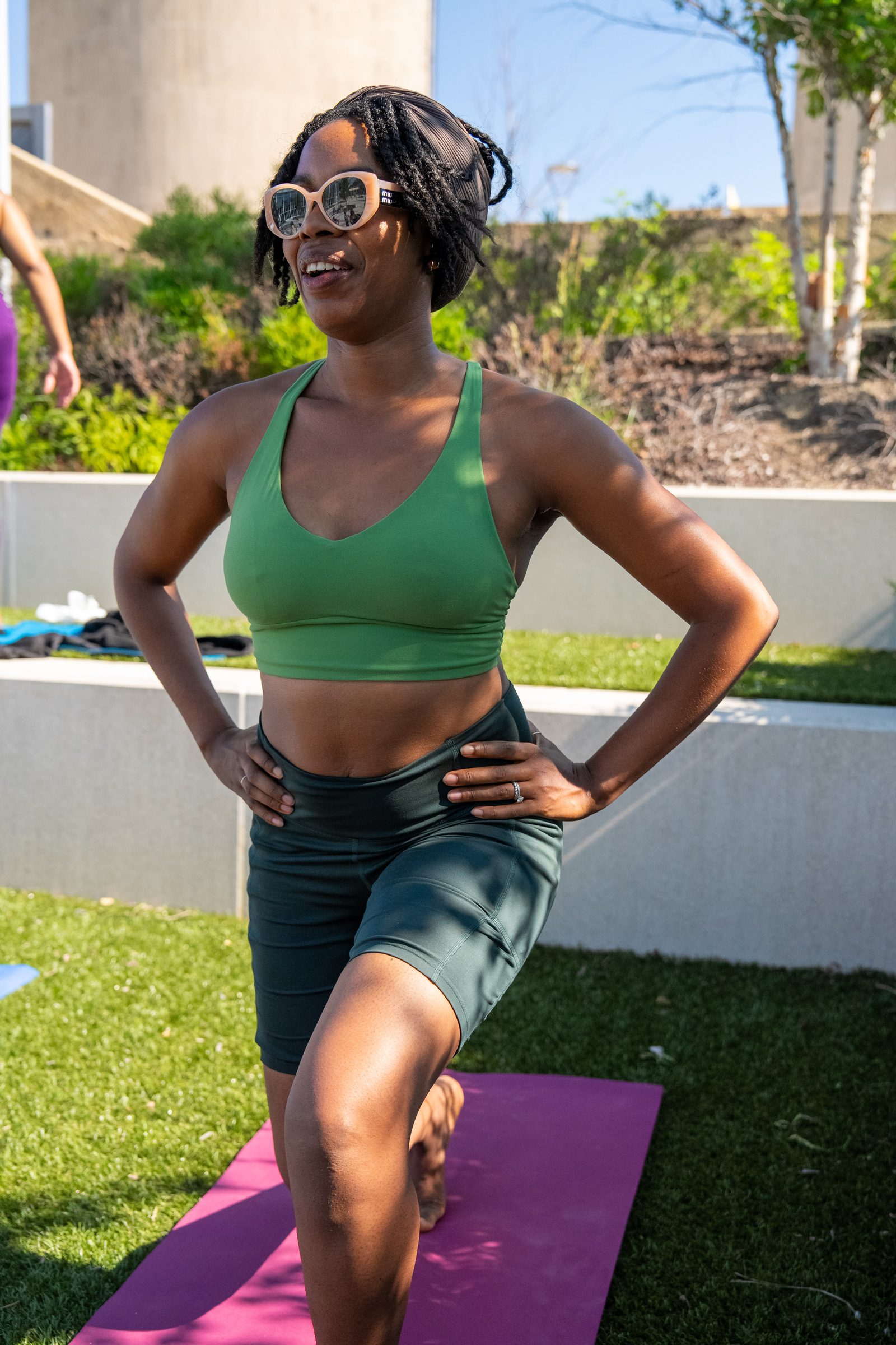 Participant in green mid-lunge, smiling, hands on hips
