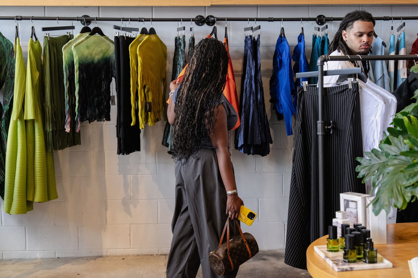 Wide view of the Ron David studio: pleated garments on racks with a customer browsing