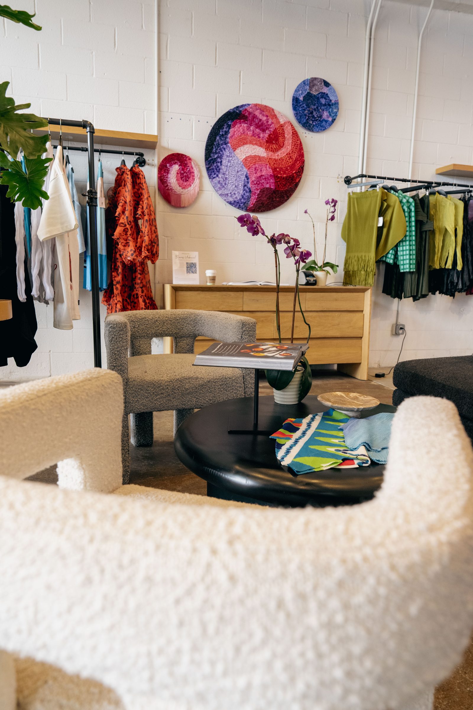 The Ron David studio: bouclé lounge chairs, textile art on the walls, clothing racks flanking the seating area