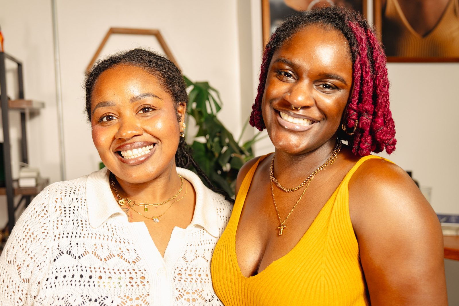 Two women smiling at the camera, warm salon light behind them